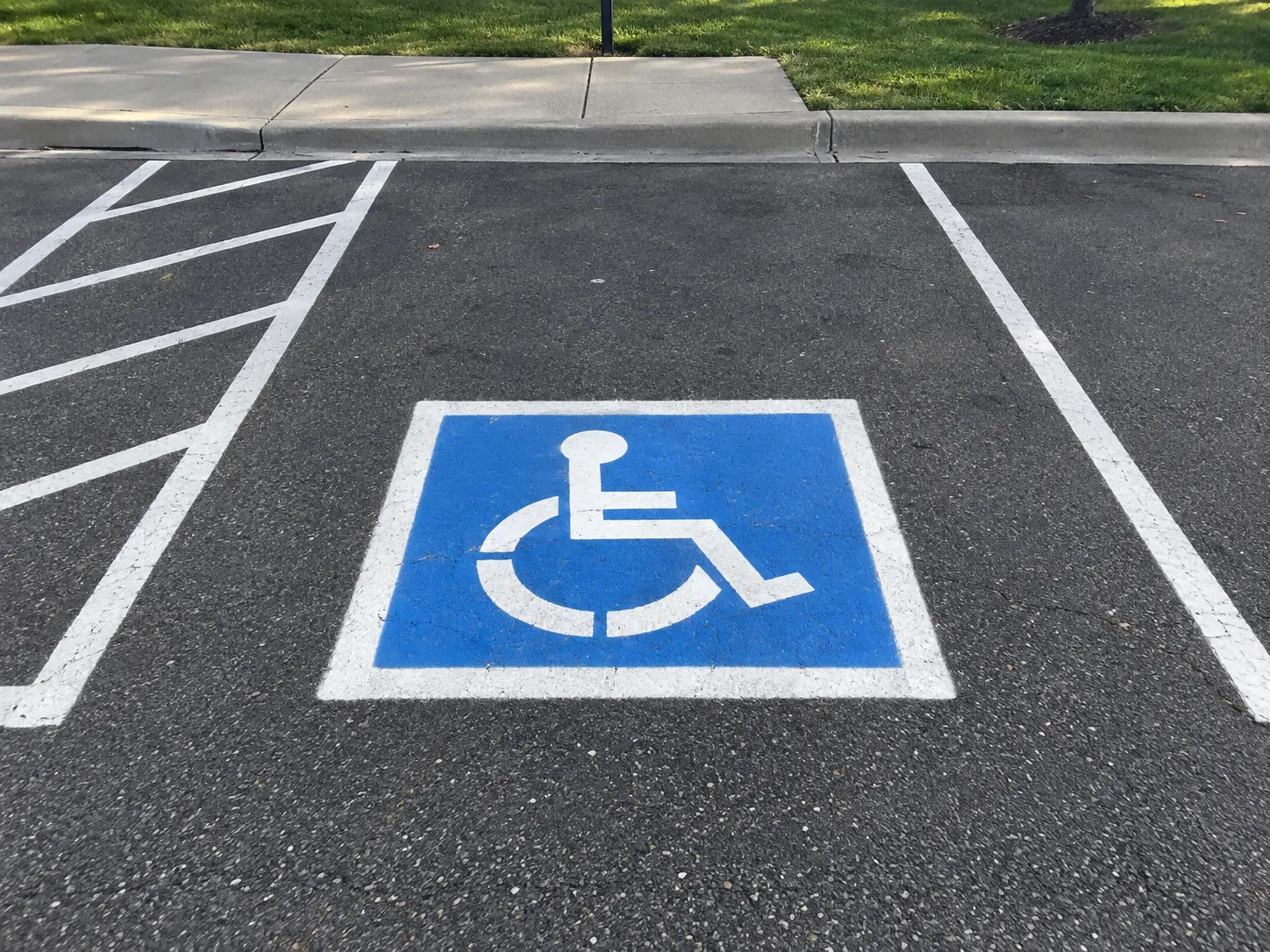 Blue and white ADA accessible parking space with a cross-hatched access aisle next to a sidewalk